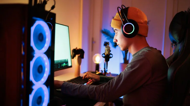 Человек сидит за освещенным настольным компьютером в наушниках RGB.