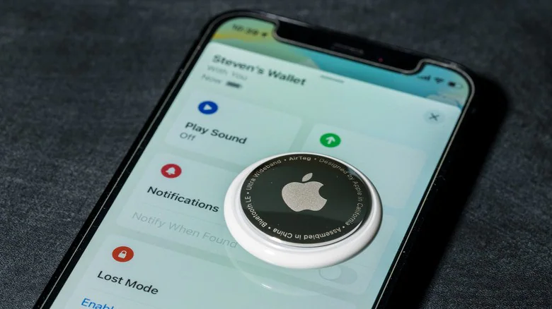 Apple AirTag задней крышкой вверх, расположенный поверх iPhone с открытым приложением Find My.
